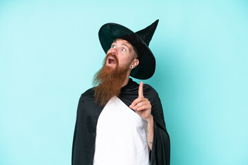 Young wizard in halloween isolated on blue background thinking an idea pointing the finger up
