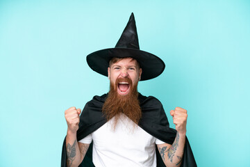 Young wizard in halloween isolated on blue background celebrating a victory in winner position