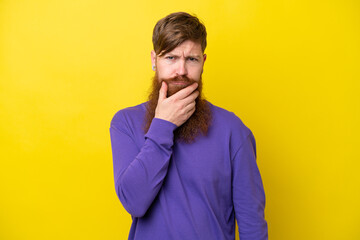 Fototapeta premium Redhead man with beard isolated on yellow background having doubts