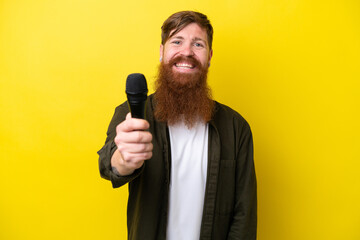 Naklejka premium Redhead man with beard picking up a microphone isolated on yellow background with happy expression