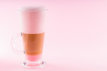 Latte macchiato with pink foam on a pink background. Latte macchiato coffee in a transparent glass. Layered coffee drink with milk. Copy space