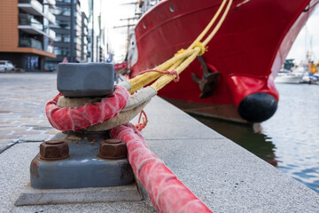 Close-up of a mooring steel post, bitteng or bitt, on a pier to which a modern ship is tied with...