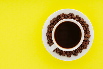 Coffee cup and roasted coffee beans on a saucer. Cup of black coffee on a yellow background. Top view. Copy space