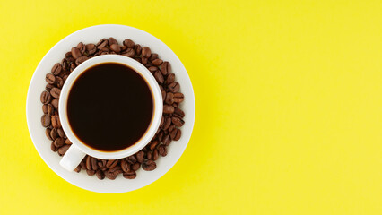 Coffee cup and roasted coffee beans on a saucer. Cup of black coffee on a yellow background. Top view. Copy space
