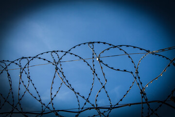 Fragment of fence made of barbed wire. Against background of blue sky. Barbed Wire Fence. Captivity, prison