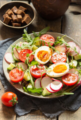 Homemade delicious vegetable salad with chicken eggs and croutons on a wooden table. Close up