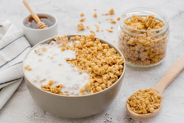 Dry breakfast cereals. Crunchy honey granola bowl and a glass of milk on a table. Healthy and fiber food.