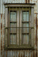 Old wooden window with a green grille in an old house with sheet metal walls.