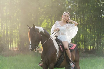 Foto op Canvas Woman riding red horse in the garden. Beautiful bride in a dress riding a horse. © Thirawatana
