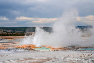 Scenic view of steam emitting from Clepsydra Geyser amidst geothermal landscape. Erupted hot spring in forest at Yellowstone national park. Famous place with cloudy sky in background.
