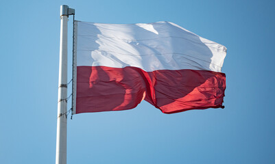 Fototapeta na wymiar Polish red and white flag in the wind. A wavy Polish flag hoisted on the mast. National colors in white and red.