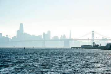 Obraz premium Scenic view of Bay Bridge and San Francisco skyline. Downtown district on sea coast with clear sky in background. Famous tourist attraction connecting urban town.