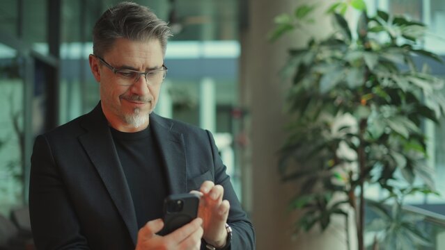 Businessman Using Phone In Office. Middle Aged Man In Business Casual, Entrepreneur Working Online, Reading Finance Report, Thinking. .