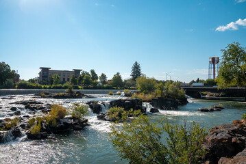 Fototapeta na wymiar Beautiful snake river at Idaho falls flowing by museum. Rapid water amidst rocks and plants with blue sky in background. Natural scenery of famous tourist attraction in city during sunny day.