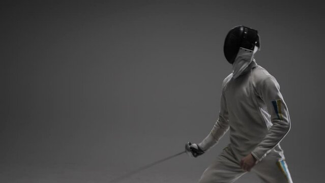 swordsman in a white protective suit, wearing a protective mask and holding a fencing foil in his hand.