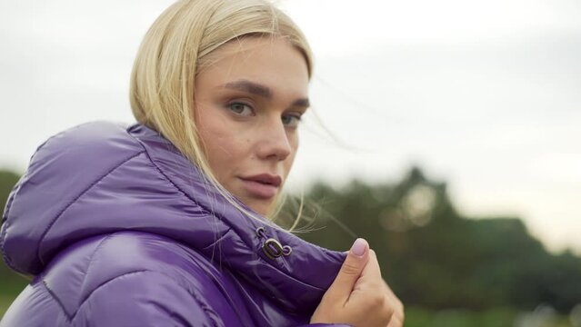 Portrait of a Caucasian model in a purple down jacket. A beautiful girl looks at the camera. Winter clothes. High quality 4k footage