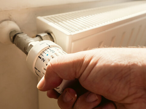 Main d'homme baissant le thermostat de son chauffage radiateur - Personne qui r&egrave;gle la temp&eacute;rature de son logement pour faire des &eacute;conomies, &agrave; cause de l'augmentation des prix de l'&eacute;nergie et du gaz