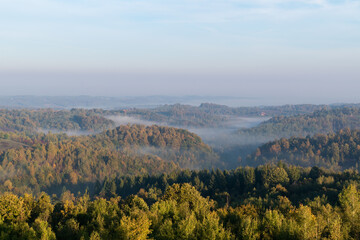 Fototapeta na wymiar Morning fog in valleys between hills in autumn, airy rural landscape with deciduous forest