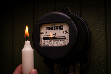 Checking old retro Russian electric meter with candle light. Energy crisis and power outage. High...
