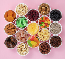 Nuts, seeds, dried fruits in round containers. Background with a mix of healthy snacks. Assorted vitamin food on a pink background.