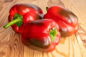 Three red organic, bell peppers, close-up, on a wooden table.