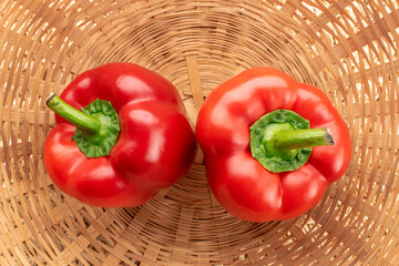 Two red bell peppers, close-up, in a straw bowl, top view.