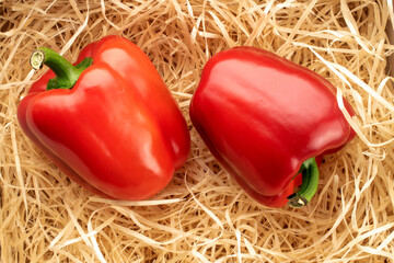 Two red bell peppers, close-up, in wood shavings, top view.