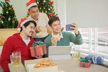close up group of asian friends using smartphone and take selfie for party group shot in living room with pine tree christmas decoration prepare for celebration festival , relationship concept