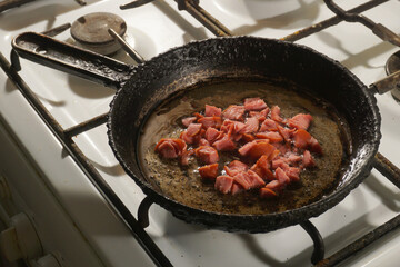 Pieces of sausage or sausages are fried in a frying pan on a gas stove.