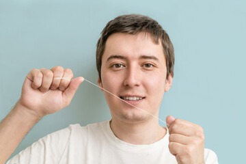 a young man brushes his teeth with dental floss for the prevention of caries on a blue background. oral hygiene, dental care