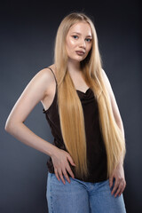 Fototapeta premium Young blonde woman in jeans and brown singlet on gray background