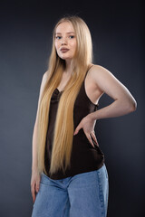 Naklejka premium Young blonde woman in jeans and brown singlet on gray background