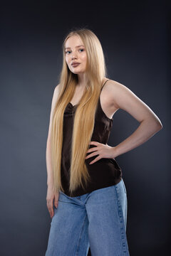 Young blonde woman in jeans and brown singlet on gray background