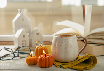 Autumn composition, hot cup of coffee, candles, candlesticks miniature house on a wooden table. Seasonal, morning hot coffee. Relaxing and still life concept. Cozy interior decor.