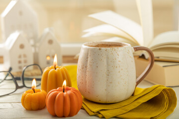 Autumn composition, hot cup of coffee, candles, candlesticks miniature house on a wooden table. Seasonal, morning hot coffee. Relaxing and still life concept. Cozy interior decor.