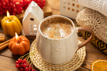 Autumn composition, a hot cup of coffee, candles, candlesticks, a miniature house and a warm sweater on a wooden table.Seasonal, morning hot coffee. Relaxing and still life concept.Cozy interior decor
