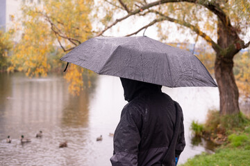 a man in a jacket with a hood, stands with his back with an umbrella in his hands, Against the...