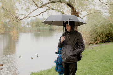 a man with a child in a jacket with a hood, stands with an umbrella in his hands, Against the...