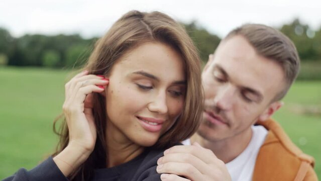 Romantic couple in love on a date in the park. A boy and a girl are sitting on the grass and hugging. Smiling happy people together. High quality 4k footage