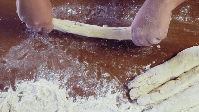 The hands of a Jewish woman form dough pieces for challah on the table. Medium plan