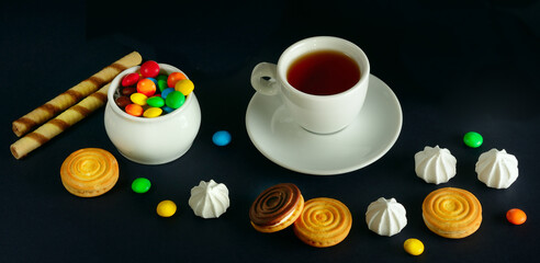Obraz na płótnie Canvas Tea cup and sweets on a black background. Wide photo.