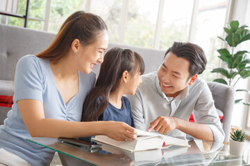Children education and home school concept : Young asian father and mother see little daughters' study. Excited smiling small child girl enjoying learning and reading with pleasant dad and mom at home
