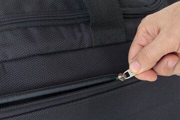hand opening the zipper of a black travel bag © OLEKSANDR
