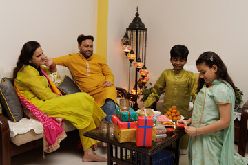 A young girl kid lighting up diya, lamp siting with family, dressed up in ethnic wear, celebrate...