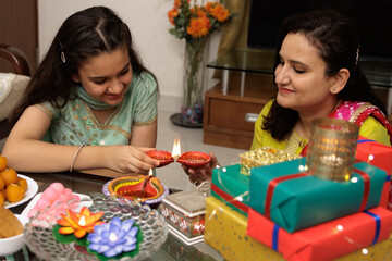 Fototapeta premium Mother and young daughter kid dressed up in ethnic wear, lighting up diya or lamp, celebrate diwali Hindu festival Laxmi poojan, kids expression