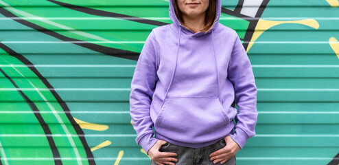 Young woman in hood in purple violet hoodie on green modern background copy space mockup friendly