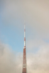 A TV tower in Riga with the antenna surrounded by clouds on a sunny morning with some blue sky