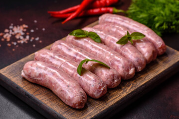 Raw sausages with ingredients on a cutting board on a dark concrete background with copy space