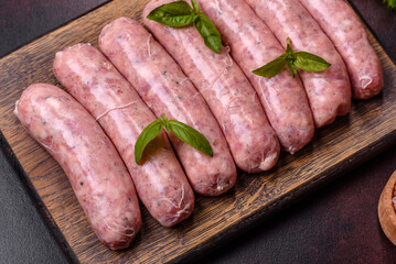 Raw sausages with ingredients on a cutting board on a dark concrete background with copy space