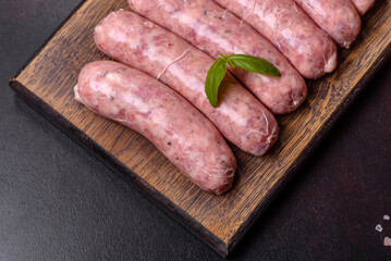 Raw sausages with ingredients on a cutting board on a dark concrete background with copy space